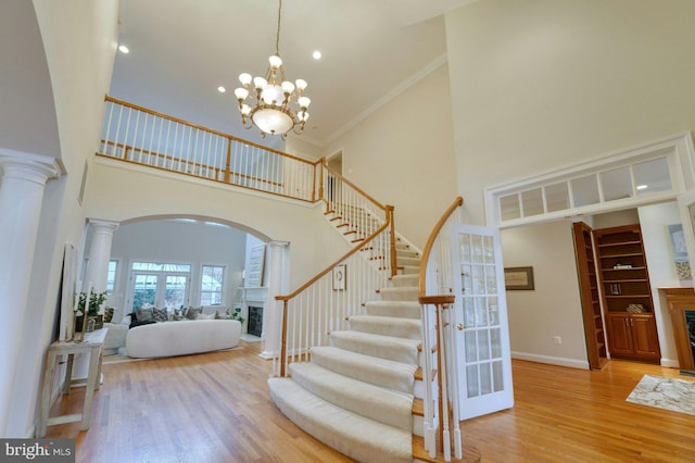 foyer entrance with a towering ceiling, decorative columns, ornamental molding, a chandelier, and light hardwood / wood-style floors