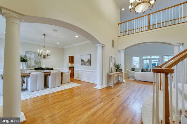 foyer with light hardwood / wood-style floors, a towering ceiling, ornamental molding, and an inviting chandelier