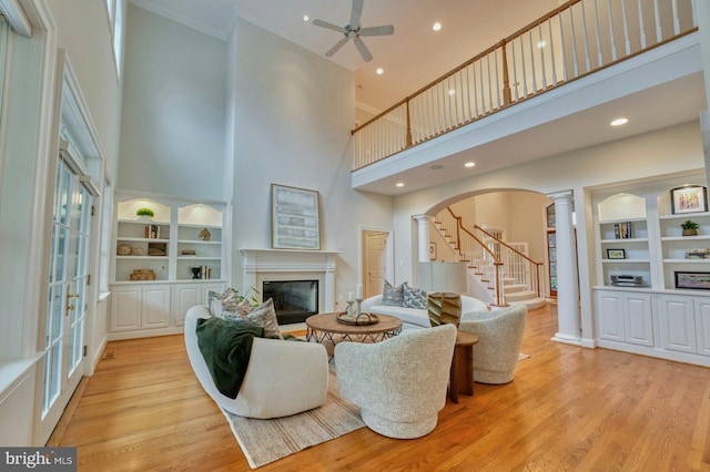 living room with ceiling fan, a towering ceiling, light hardwood / wood-style floors, and ornamental molding