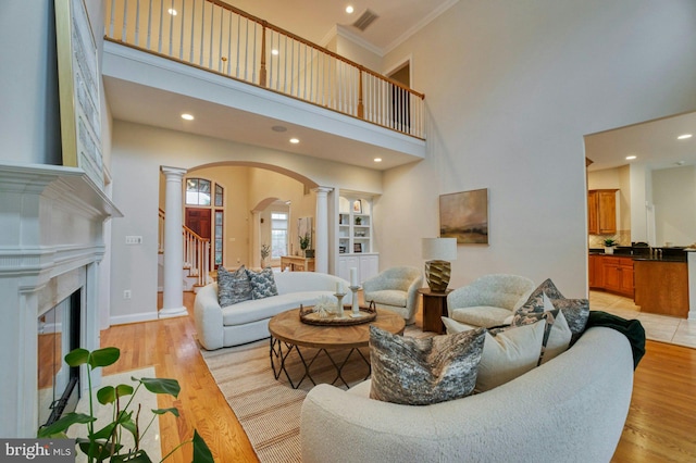 living room with decorative columns, crown molding, light hardwood / wood-style flooring, and a towering ceiling