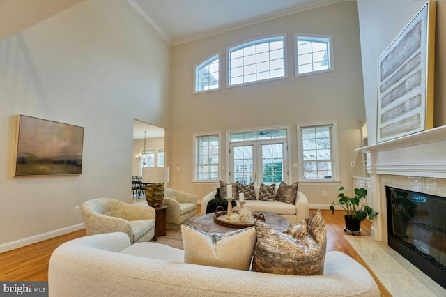 living room with light wood-type flooring, ornamental molding, ceiling fan with notable chandelier, a premium fireplace, and a high ceiling