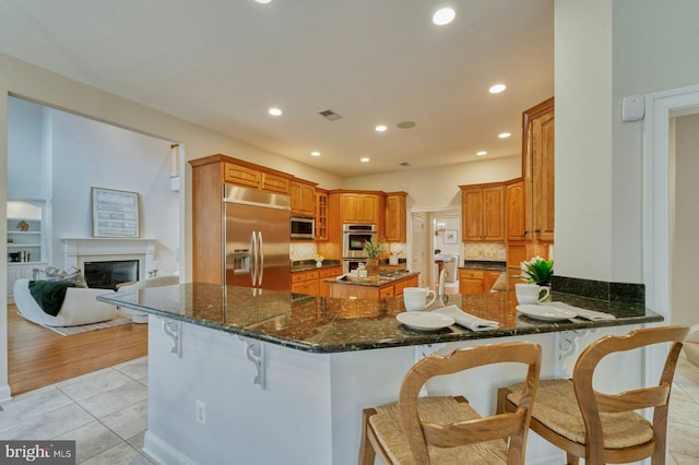 kitchen with a breakfast bar, dark stone counters, appliances with stainless steel finishes, light tile patterned flooring, and kitchen peninsula