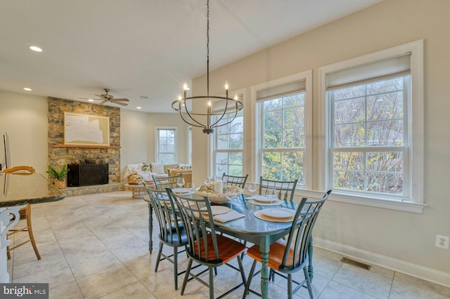 tiled dining space with ceiling fan with notable chandelier and a fireplace