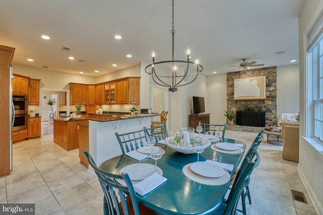 dining space featuring ceiling fan with notable chandelier, light tile patterned flooring, and a fireplace