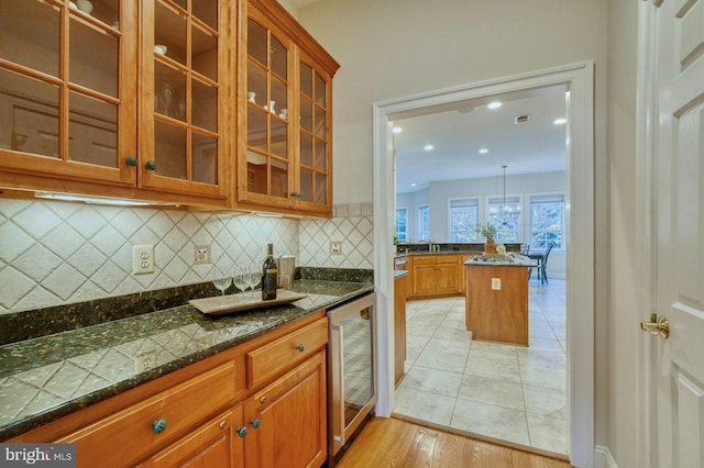 kitchen with decorative backsplash, light wood-type flooring, beverage cooler, dark stone countertops, and hanging light fixtures