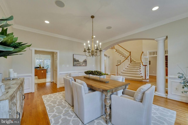 dining room featuring an inviting chandelier, light hardwood / wood-style flooring, crown molding, and ornate columns