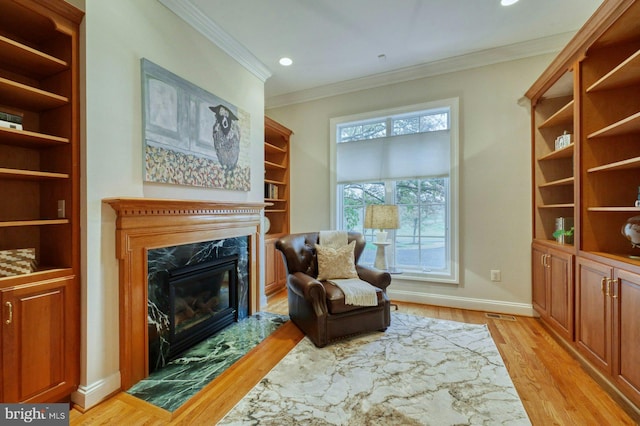 sitting room featuring light wood-type flooring, crown molding, and a premium fireplace