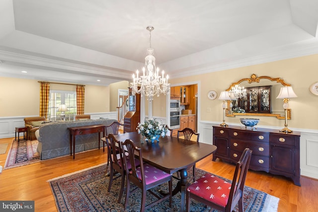 dining area featuring a tray ceiling, ornamental molding, light hardwood / wood-style floors, and a notable chandelier