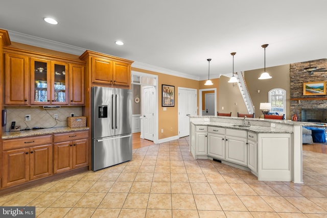 kitchen featuring a stone fireplace, light stone counters, stainless steel refrigerator with ice dispenser, light tile patterned floors, and ornamental molding