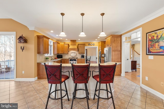 kitchen with custom exhaust hood, a center island with sink, appliances with stainless steel finishes, light stone counters, and a breakfast bar area