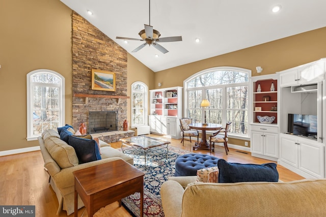 living room with a stone fireplace, ceiling fan, light hardwood / wood-style flooring, and high vaulted ceiling