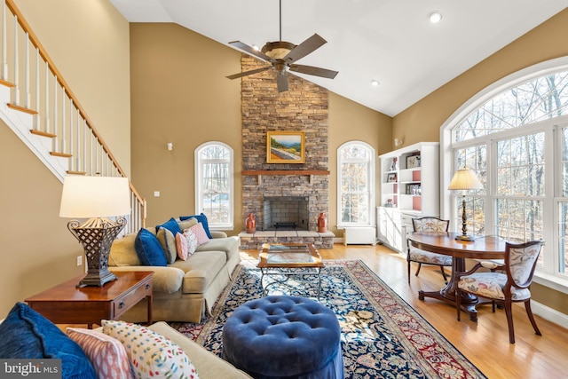 living room featuring ceiling fan, light wood-type flooring, a fireplace, and high vaulted ceiling