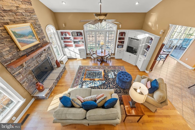 living room with ceiling fan, a fireplace, a towering ceiling, and light hardwood / wood-style floors