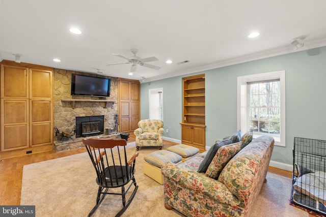 living room featuring ceiling fan, light hardwood / wood-style floors, a wood stove, and crown molding