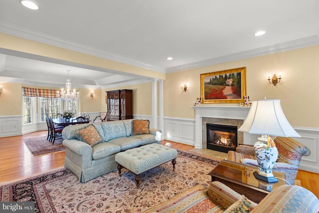 living room featuring ornate columns, light hardwood / wood-style flooring, crown molding, and a premium fireplace