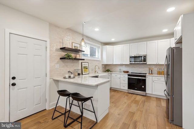 kitchen with white cabinetry, appliances with stainless steel finishes, pendant lighting, light hardwood / wood-style floors, and kitchen peninsula