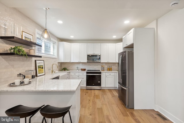 kitchen with white cabinetry, appliances with stainless steel finishes, decorative light fixtures, light wood-type flooring, and kitchen peninsula