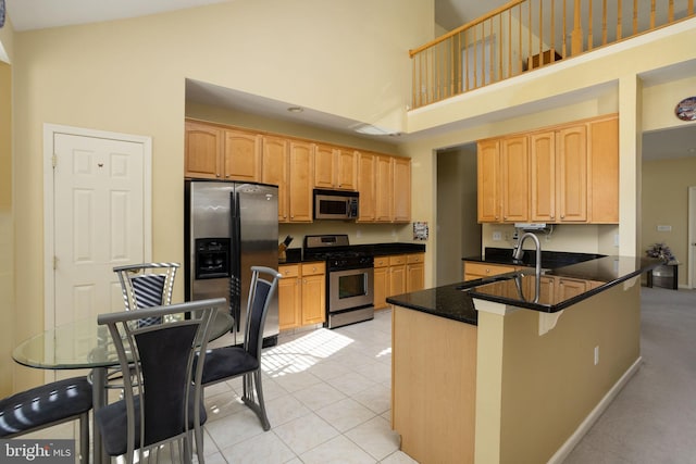 kitchen with appliances with stainless steel finishes, high vaulted ceiling, sink, light tile patterned floors, and kitchen peninsula