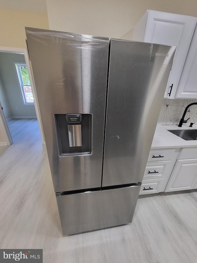 kitchen with light hardwood / wood-style flooring, white cabinets, sink, and stainless steel fridge