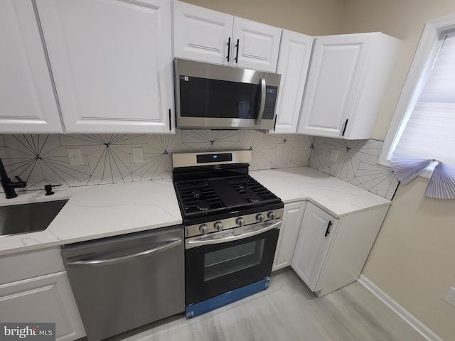 kitchen with white cabinetry, stainless steel appliances, light stone counters, backsplash, and light wood-type flooring