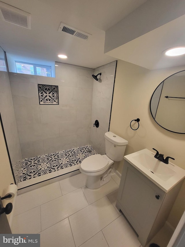 bathroom with tile patterned flooring, vanity, tiled shower, and toilet