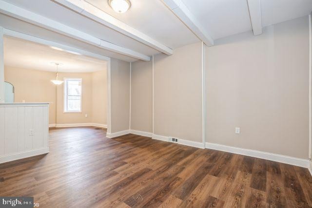 unfurnished room with dark hardwood / wood-style flooring and beamed ceiling