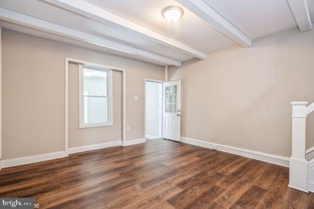 spare room with dark hardwood / wood-style floors and beam ceiling