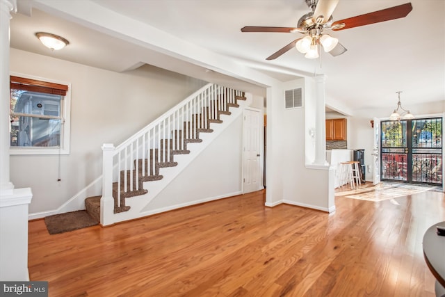 interior space with decorative columns, light hardwood / wood-style floors, and ceiling fan with notable chandelier