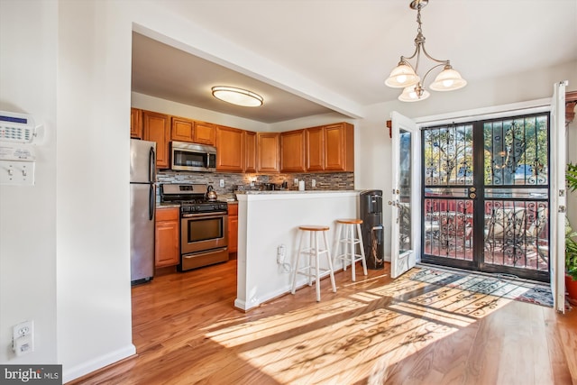 kitchen with a notable chandelier, light wood-type flooring, stainless steel appliances, and tasteful backsplash