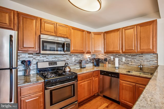 kitchen with light stone countertops, appliances with stainless steel finishes, decorative backsplash, sink, and light hardwood / wood-style floors