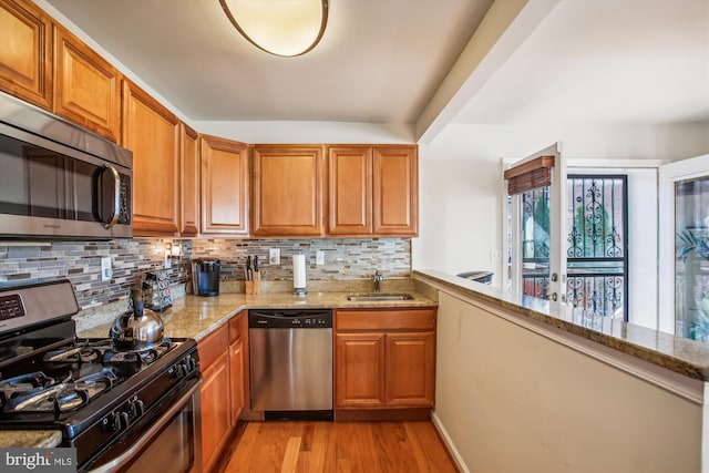 kitchen with sink, light stone counters, backsplash, appliances with stainless steel finishes, and light wood-type flooring