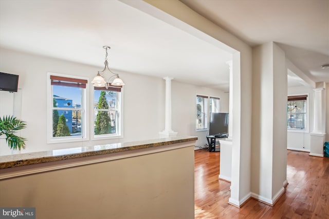 corridor featuring a notable chandelier, wood-type flooring, and decorative columns