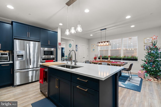 kitchen featuring pendant lighting, a center island with sink, sink, light hardwood / wood-style flooring, and stainless steel appliances