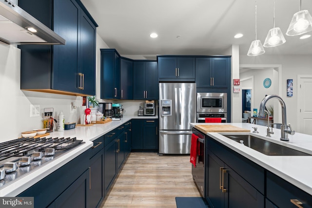 kitchen featuring appliances with stainless steel finishes, sink, exhaust hood, pendant lighting, and light hardwood / wood-style floors