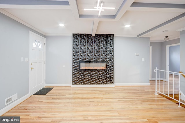 entrance foyer with hardwood / wood-style floors, a stone fireplace, and ornamental molding