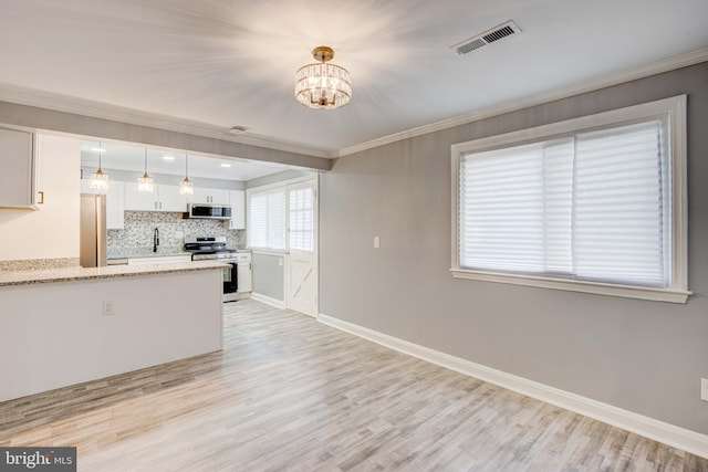 kitchen featuring white cabinets, stainless steel appliances, decorative light fixtures, and light hardwood / wood-style floors