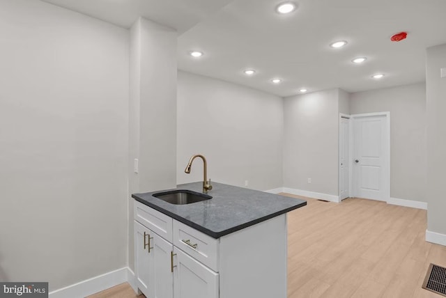 kitchen featuring white cabinets, light wood-type flooring, kitchen peninsula, and sink