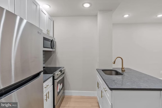 kitchen with white cabinets, sink, light wood-type flooring, kitchen peninsula, and stainless steel appliances