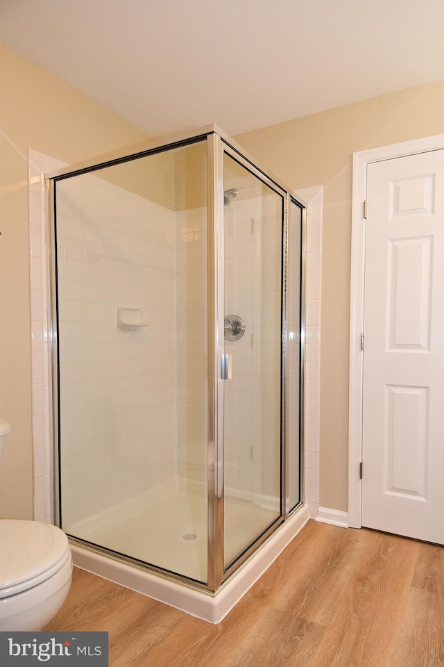 bathroom with hardwood / wood-style flooring, toilet, and a shower with shower door