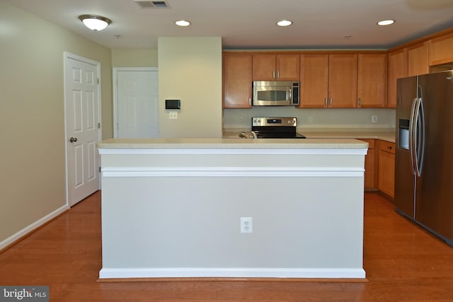 kitchen with wood-type flooring, appliances with stainless steel finishes, and an island with sink