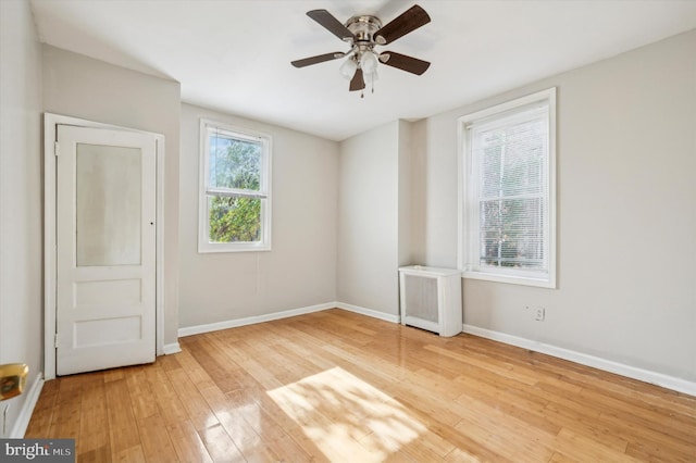 unfurnished room with ceiling fan, radiator heating unit, and light wood-type flooring