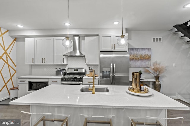 kitchen with appliances with stainless steel finishes, white cabinetry, a breakfast bar area, and wall chimney range hood