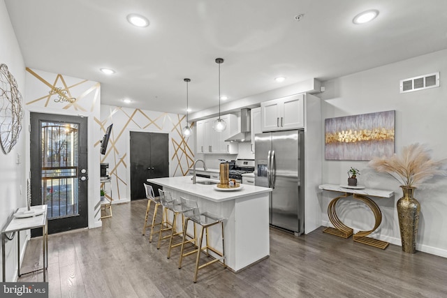 kitchen with appliances with stainless steel finishes, wall chimney range hood, decorative light fixtures, white cabinets, and dark hardwood / wood-style floors