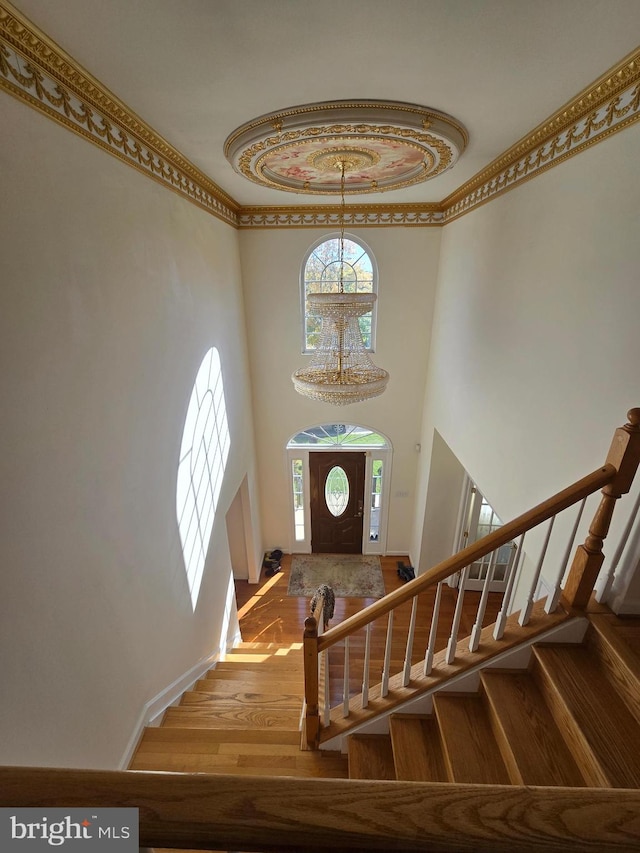 foyer entrance featuring light wood-type flooring, ornamental molding, and a towering ceiling