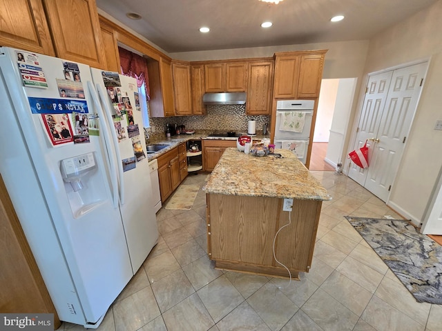 kitchen with white appliances, sink, decorative backsplash, light stone countertops, and a kitchen island