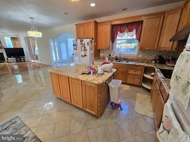 kitchen with light stone countertops, hanging light fixtures, tasteful backsplash, white refrigerator with ice dispenser, and a kitchen island