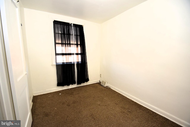 empty room featuring dark colored carpet and baseboards