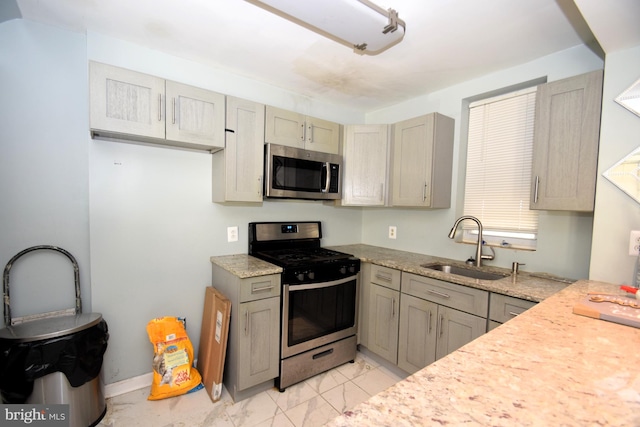 kitchen featuring light stone counters, marble finish floor, appliances with stainless steel finishes, a sink, and baseboards