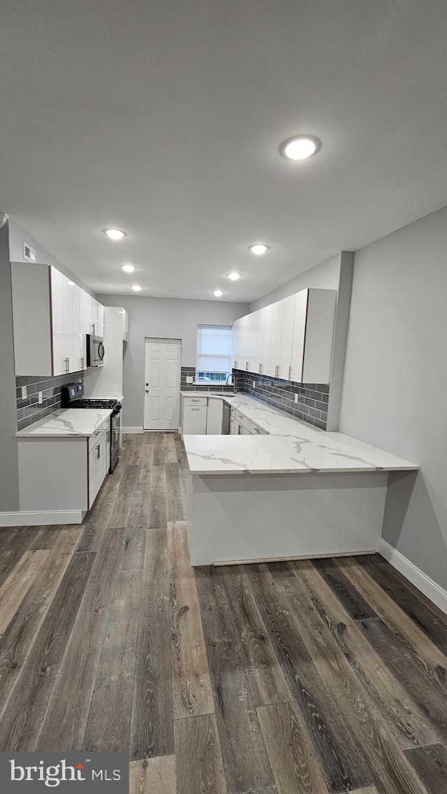 kitchen with appliances with stainless steel finishes, kitchen peninsula, tasteful backsplash, white cabinets, and dark wood-type flooring