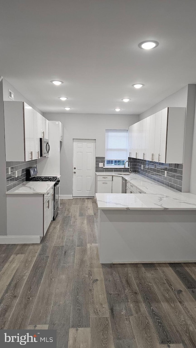 kitchen with white cabinetry, appliances with stainless steel finishes, decorative backsplash, dark wood-type flooring, and kitchen peninsula